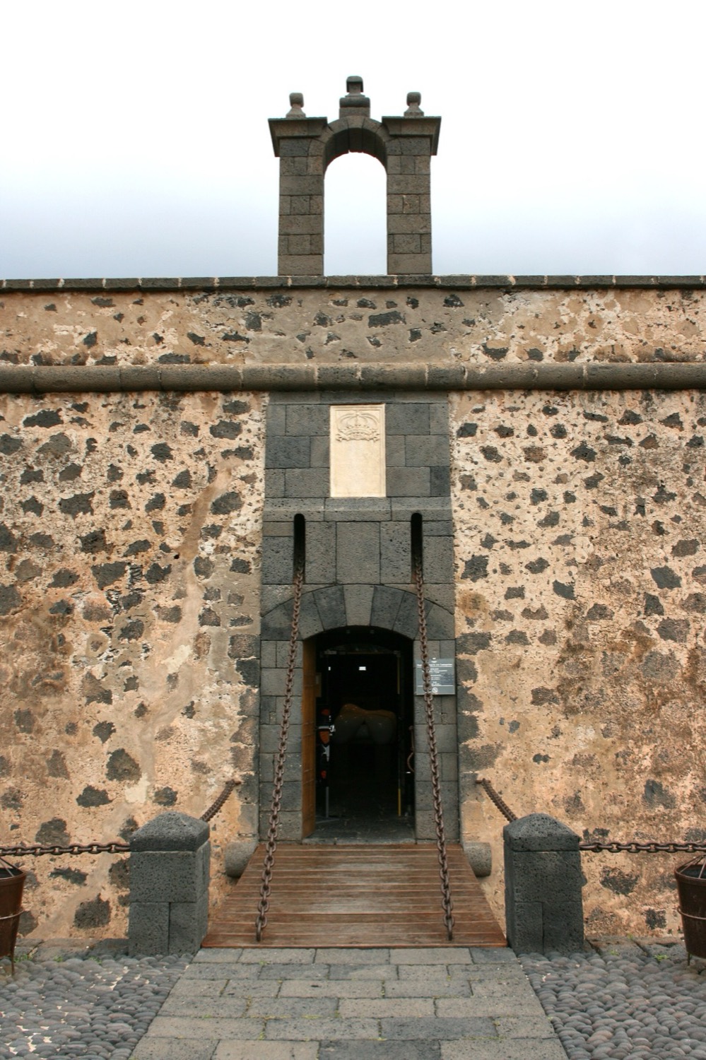 Portada de piedra del Castillo de San José, en Arrecife, con su pequeña espadaña y el puente de madera que lleva a la entrada.