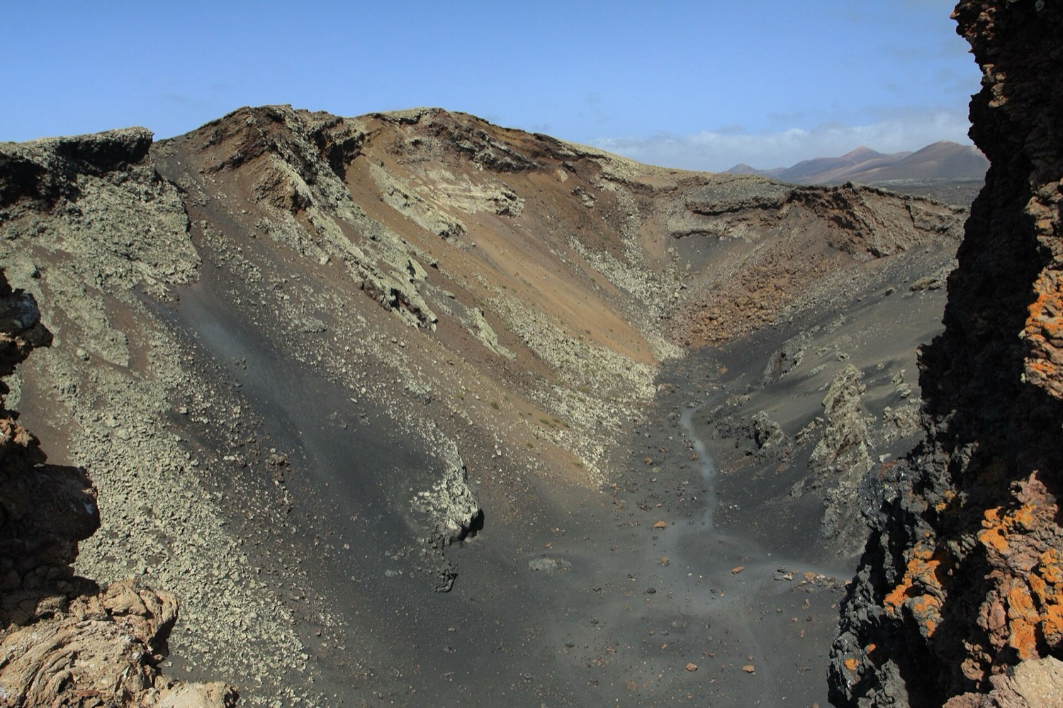 Interior de la Caldera de los Cuervos visto desde el borde: paredes de lapilli ocre y negro, fondo de picón y roca rojiza en primer plano.