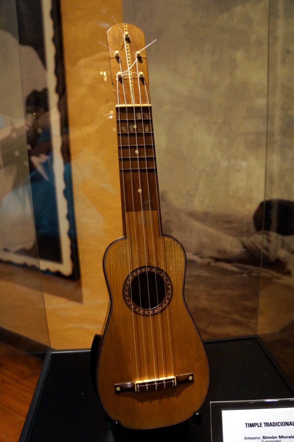 Un timple tradicional de madera clara y cinco cuerdas, expuesto en una vitrina de la Casa-Museo del Timple de Teguise.