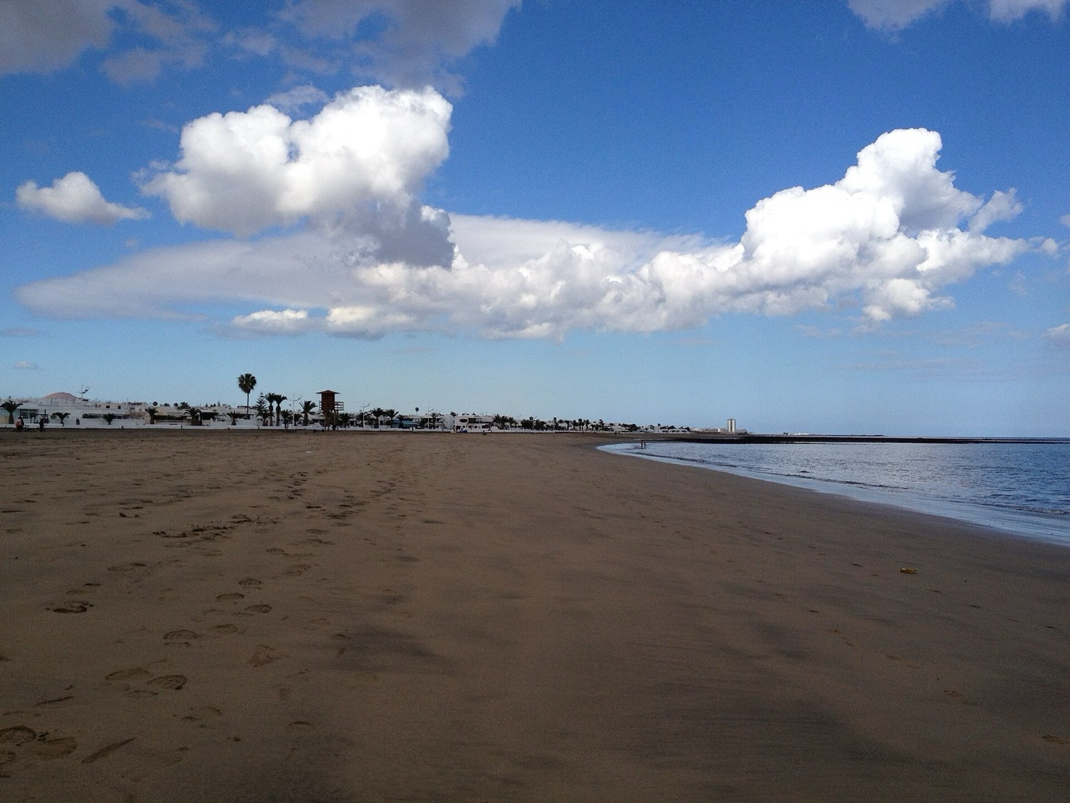 La playa de Guacimeta, en Playa Honda: arena oscura y amplia, mar en calma y nubes blancas sobre la costa.
