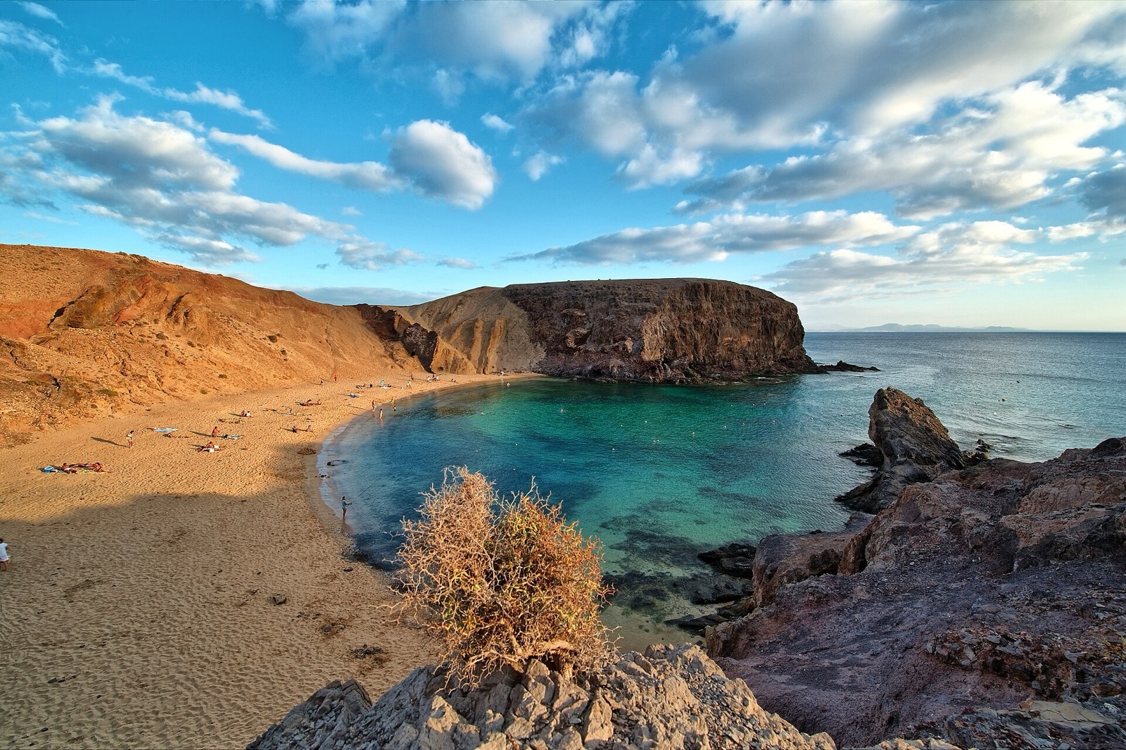 Playa del Papagayo: arena dorada, agua turquesa y acantilados ocres bajo un cielo de nubes altas, en el sur de la Reserva de la Biosfera.