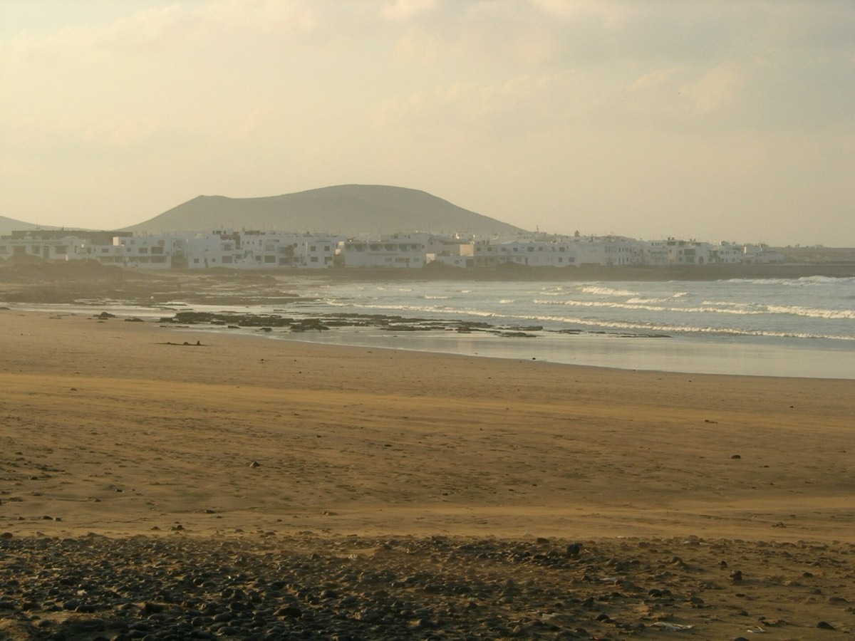 Playa de Famara al atardecer, con las casas de la urbanización y el mar de fondo