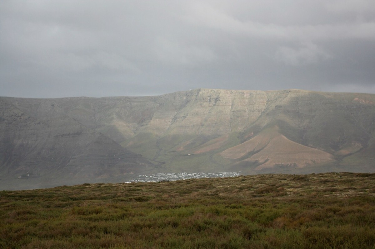 El Risco de Famara visto desde Caleta de Famara, con el pueblo blanco a sus pies bajo un cielo gris