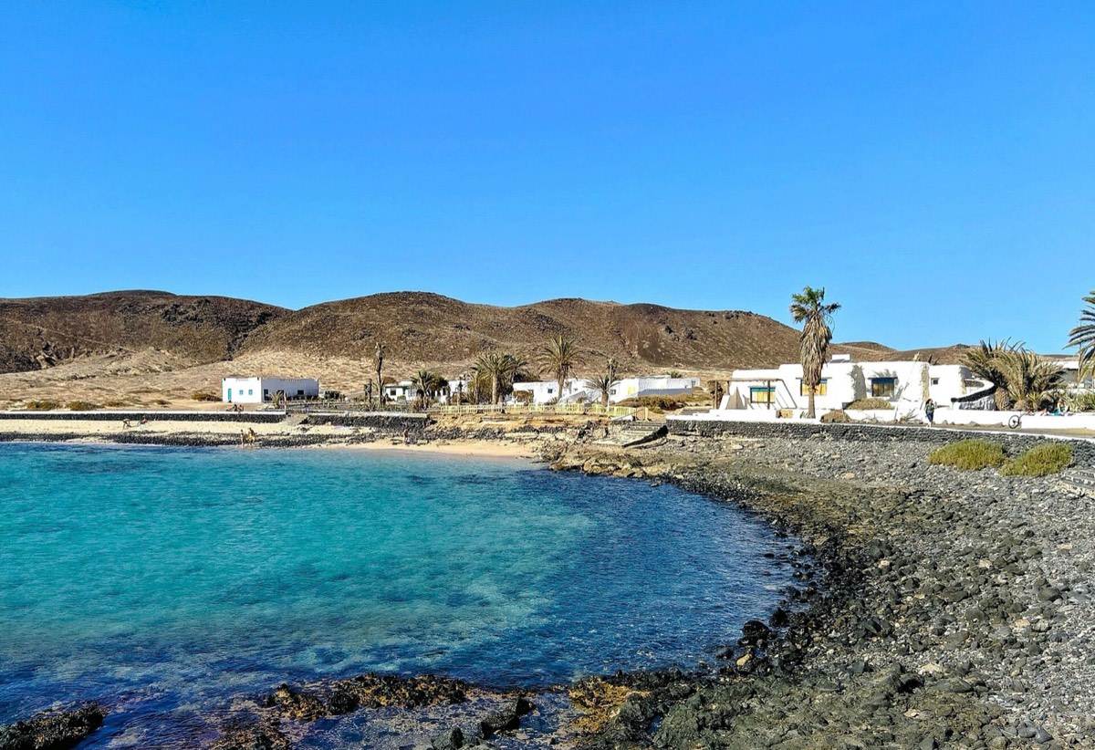 La cala de Pedro Barba, con casas blancas, palmeras y agua turquesa sobre roca oscura