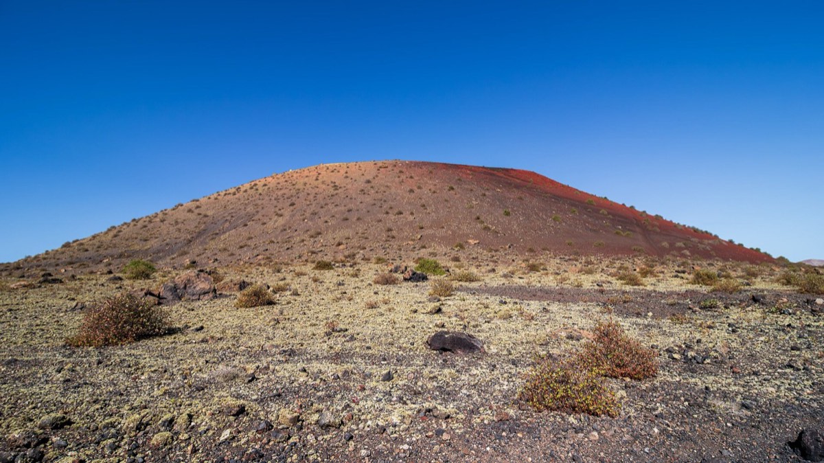 Cono rojizo de Montaña Colorada sobre un llano de lava con matorral, en el Parque Natural de Los Volcanes