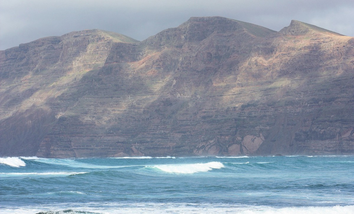 El risco de Famara visto desde la orilla de la Caleta, con olas en primer plano