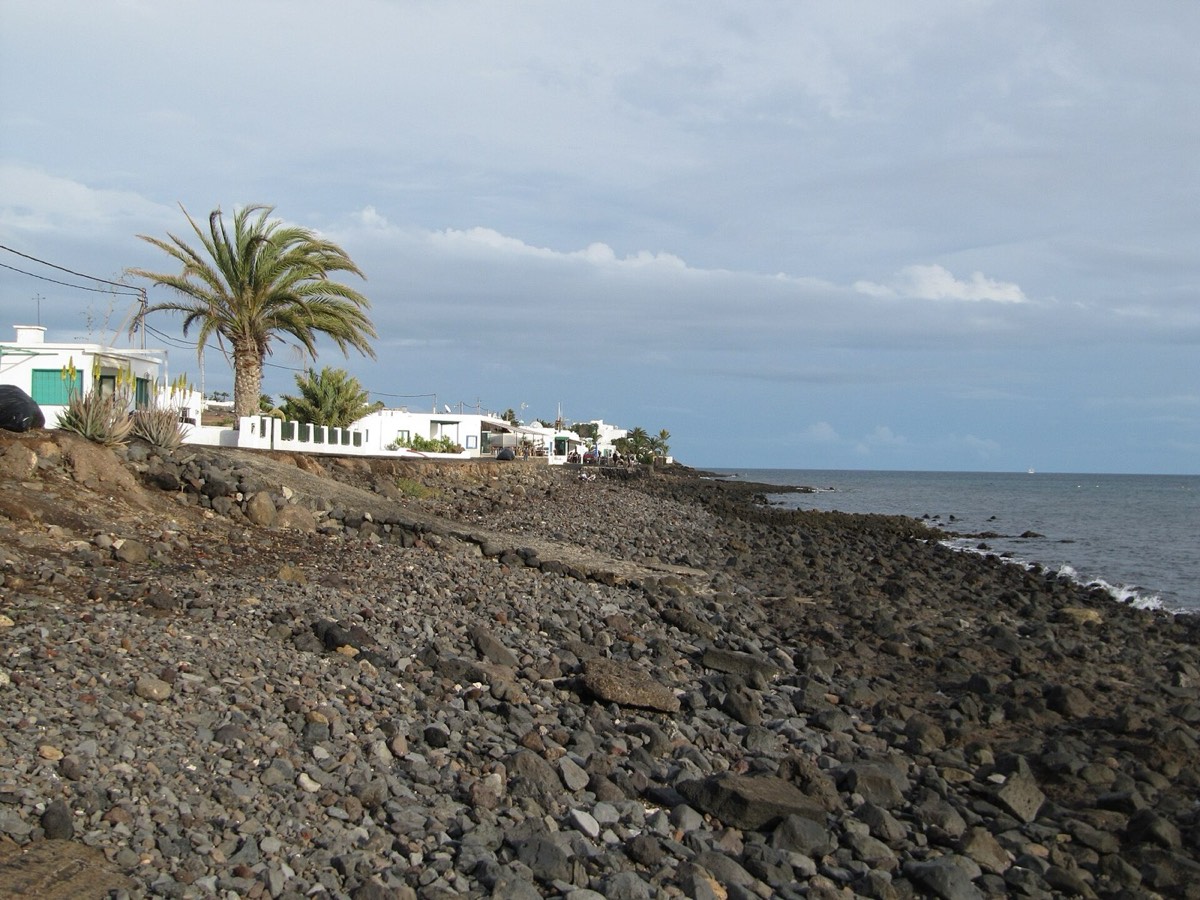 Casas blancas y orilla de callaos oscuros en Playa Quemada